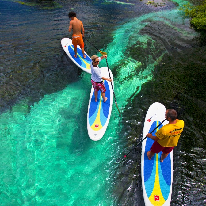 Three people paddle board over reef