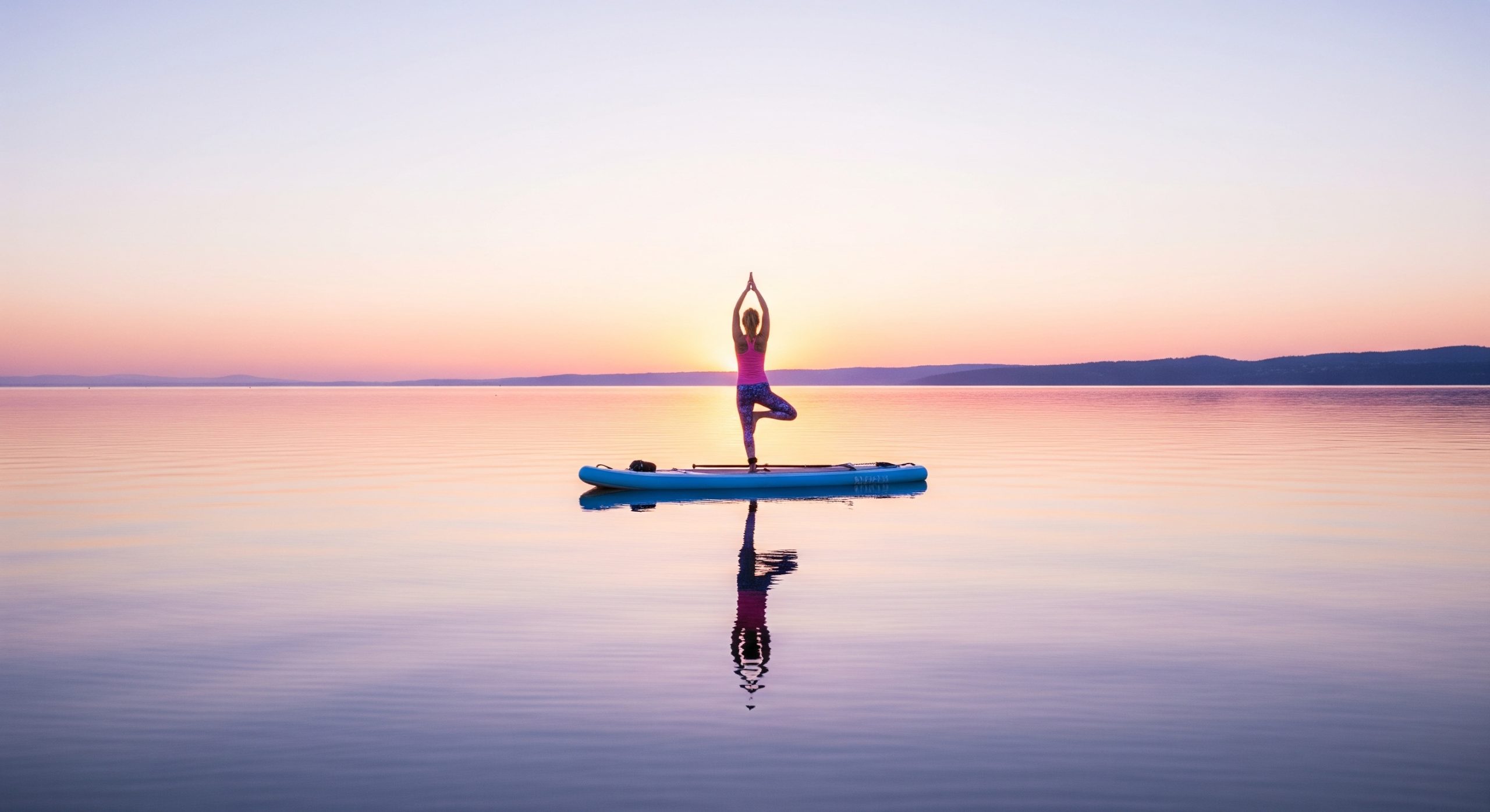 A woman doing yoga on a wide inflatable paddleboard on calm water at sunrise